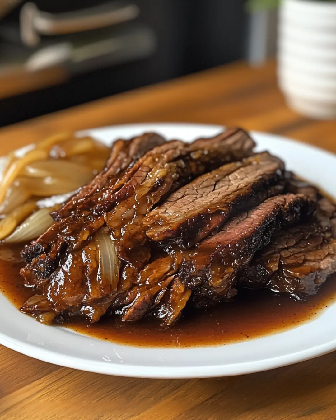Tender sliced brisket with caramelized onions and rich sauce on a white plate, showing the result of brisket injection in a slow cooker.
